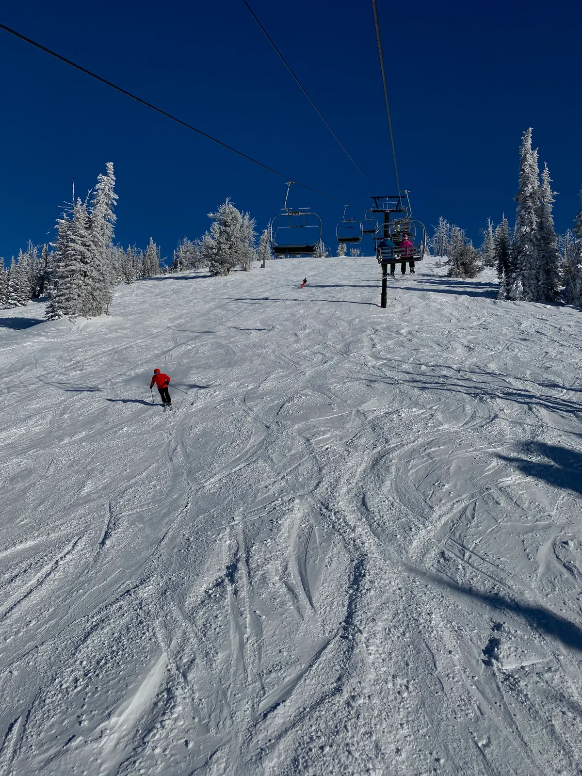 Skier on a groomed run below the chairlift under a deep blue sky