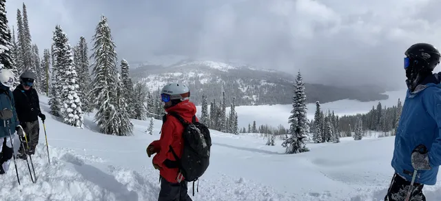 Skiers looking out over a snowy valley from the top of a run