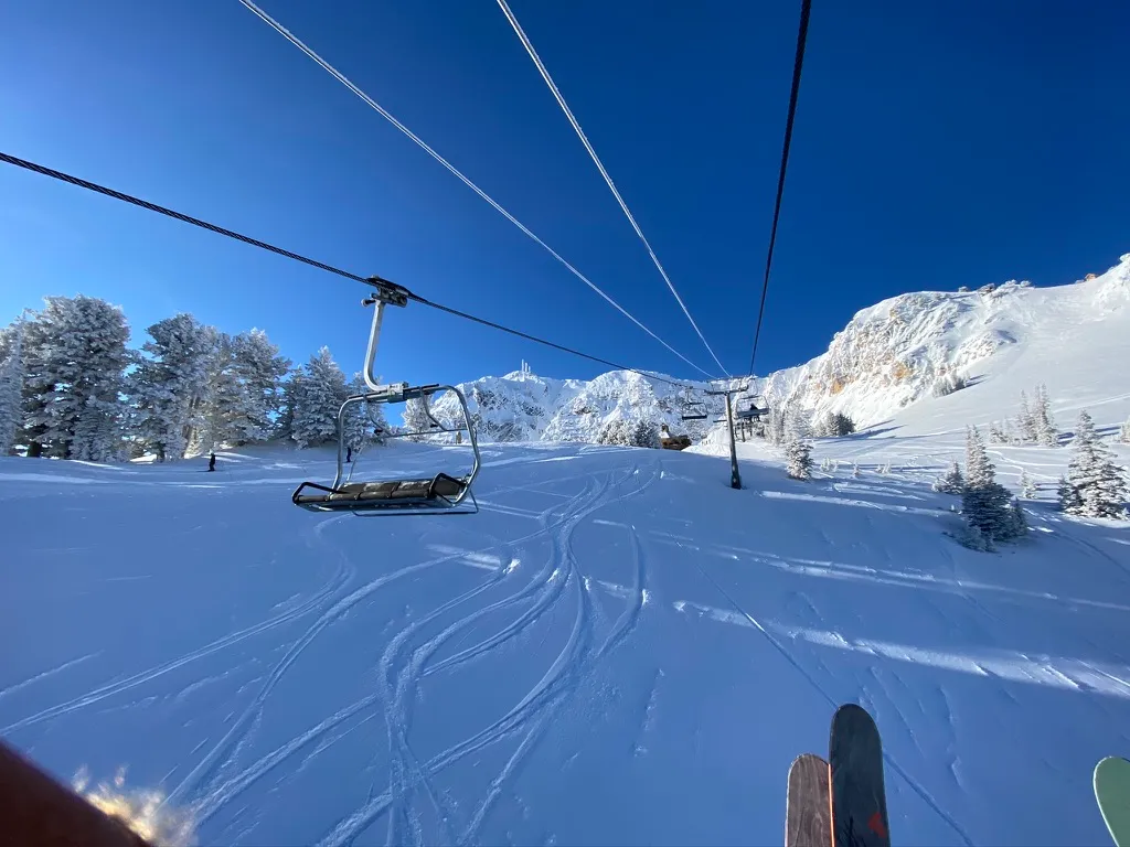 View from a chairlift over tracked snow toward a rocky ridge