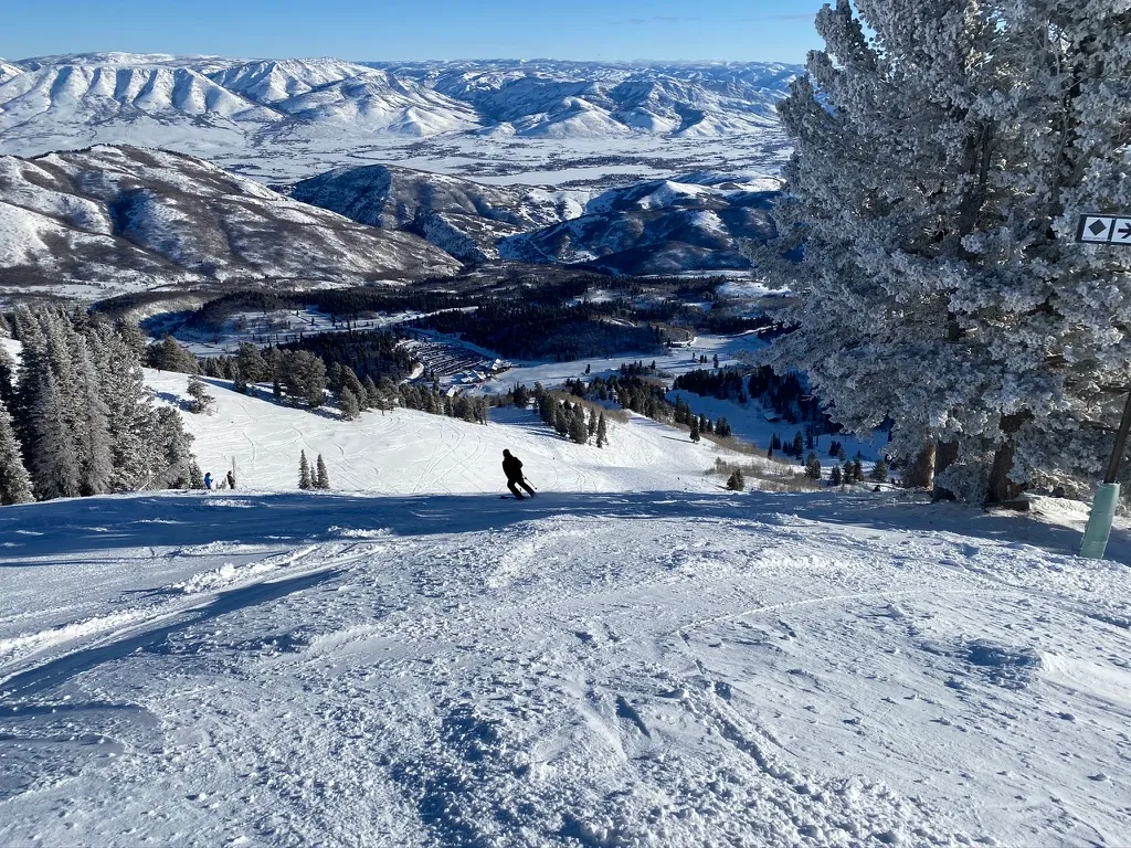 Skier on a groomed run with the valley and mountains below